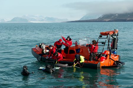 Crew John Chambers and Crew David Reichert film in the water next to the FRC, as Eric Ste-Marie, Aldo Kane, Nigel Hussey, Melissa Marquez, Crew Josh Palmer, and Cameraman Jamie Holland ride in boat while tagging a Greenland Shark. (National Geographic/Mario Tadinac)
