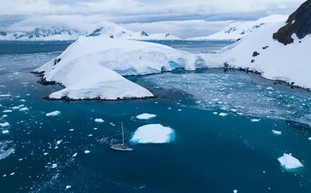 The Spirit of Sydney sailing along the coastline past a large iceberg.  (credit: National Geographic/Bertie Gregory)