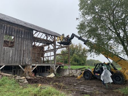 Ben Reinhold and Charles Pol, on a lift, carefully take down a historic barn in the rain, as crew members film them. (National Geographic)