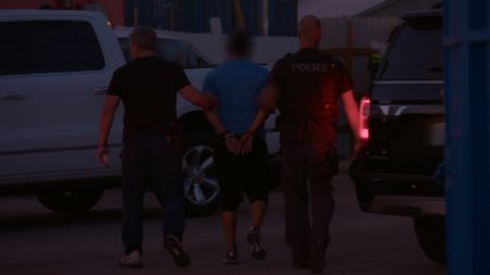 Two HSI agents lead a suspect away in handcuffs after following them during an operation in Miami, Fla. (National Geographic)