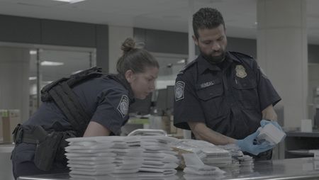 CBP Officer Griffin looks on as CBP Officer Hundal inspects multiple electronic devices found in a courier's belongings in Dulles, Va. (National Geographic)