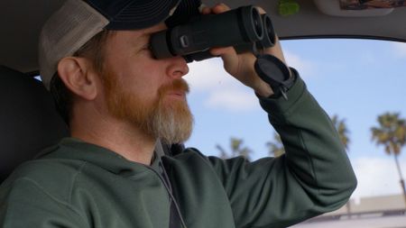 HSI Agent Connor is using binoculars in order to get better eyes on a suspect during an operation. (National Geographic)