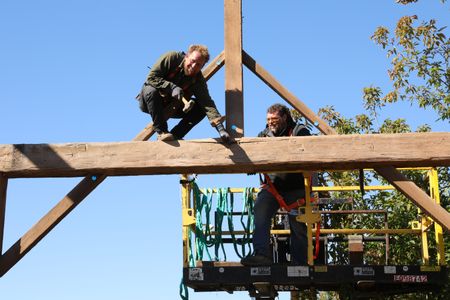 Ben Reinhold smiles while taking down the beams from the old barn as Charles Pol assists him from a lift. (National Geographic)