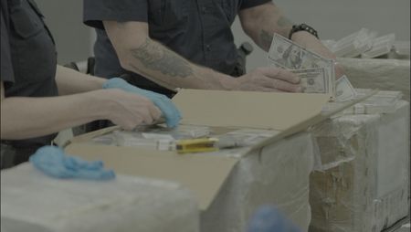 CBP Officers Pirollo and Johnson count and inspect stacks of counterfeit currency they discovered inside a shipment in Philadelphia. (National Geographic)