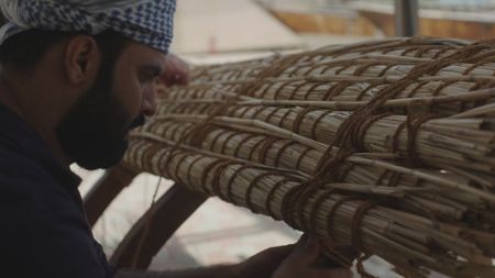 Craftsman Ayaz Al-Zadjali examines the beginnings of a reed crafted raft in Qantab, Oman. (Windfall Films)