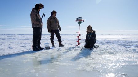 Avery and Gage Hoffman teach their cousin Jaxon how to drill a hole in the ice for ice fishing. (BBC Studios/Brian Bitterfeld)