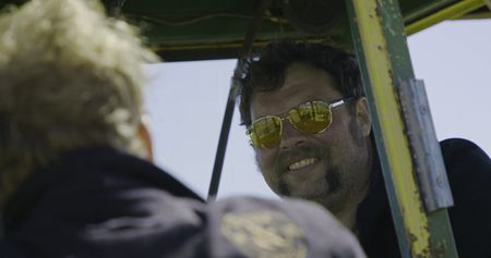 Relieved, Charles Pol listens to Ben Reinhold from inside the green tractor after they have just managed to get the tractor unstuck in the mud. (National Geographic)