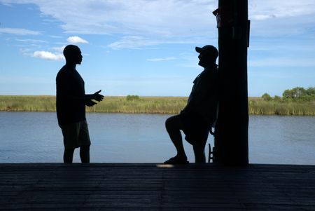 Silhouetted with the estuary marsh habitat in the background, Anthony Mackie chats with scientist Dr. Marcus Drymon on the dock of Lake Pontchartrain. (National Geographic/Brian Roedel)