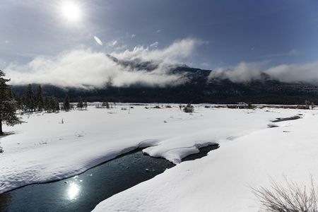 A sunny valley covered in a thick layer of snow with a slow stream cutting through it.  (National Geographic/Thomas Winston)