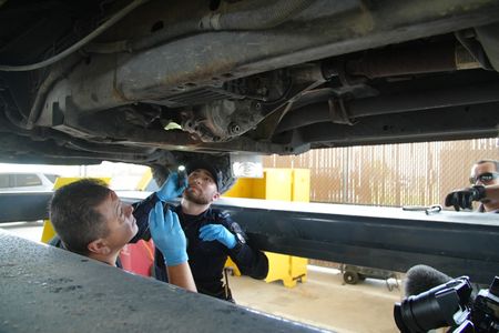 CBP Officers Rodriguez, Thomas, and Vasquez use tools to inspect the underside of a suspect's vehicle for smuggled narcotics in Pharr, Texas. (National Geographic)