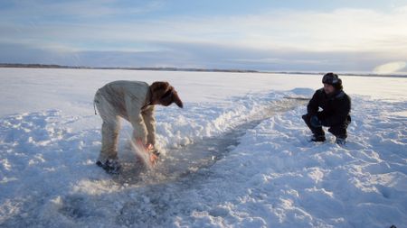 Gage Hoffman cuts holes through the ice so his brother Avery can help him set a fish net. (BBC Studios/Danny Day)