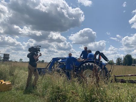 A crew member films Dr. Pol, Ben Reinhold, and Charles Pol getting the blue tractor ready to condition the hay at the Pol family's farm. (National Geographic)