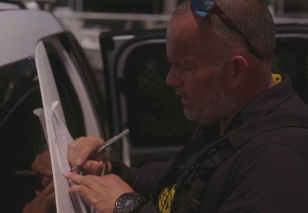 A CBP Agent is writing on a paper against the side of a vehicle in Fajardo, PR. (Lucky 8 TV)