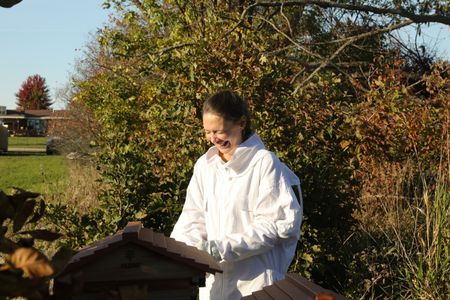 Beth Pol, in a bee suit, laughs while checking on the bees at the Pol family's farm to make sure they are ready for winter. (National Geographic)