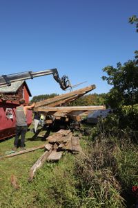 Scott Brady, Charles Pol, and Bill Klein guide the telehandler as it lowers lumber from the old barn onto the ground. (National Geographic)
