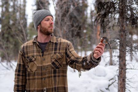 Johnny Rolfe holds a piece of meat as a chickadee tries to take it. (BBC Studios Reality Production/Patrick Henderson)