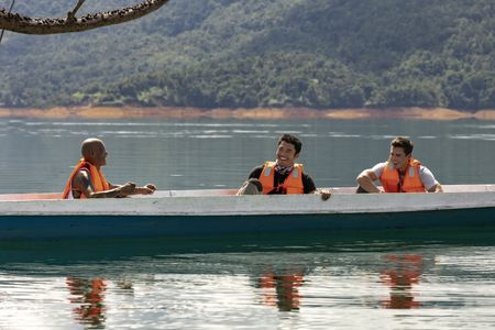 Henry Golding and Antoni Porowski learn about Iban history from a guide as they tour the river in Bantang Ai. (Credit: National Geographic/Annice Lyn)