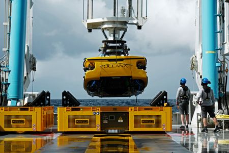 A submarine is lifted by a crane from the deck of the OceanXplorer. (National Geographic/Mario Tadinac)