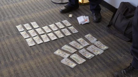 Multiple stacks of currency were placed on the ground after they were discovered in a passenger's belongings in Dulles, Va. (National Geographic)