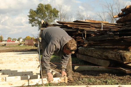 Ben Reinhold pulls apart a frame from the old barn, next to a pile of lumber at the Pol family's farm. (National Geographic)