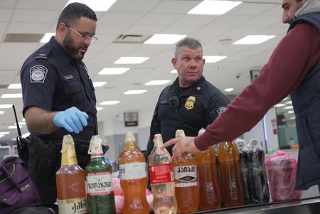 CBP Officers De La Cruz and Adams discuss what to do about multiple bottles of homemade wine found in a traveler's luggage  at the Philadelphia International Airport in Philadelphia, Pa.  (National Geographic)