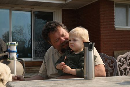 Charles Pol sits and drinks coffee outside on his deck, with his son Silas Pol on his lap. (National Geographic)