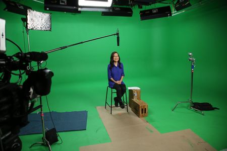 Helen Hong smiling and sitting Infront of a green screen surrounded by audio and visual equipment. (National Geographic/Robert Toth)