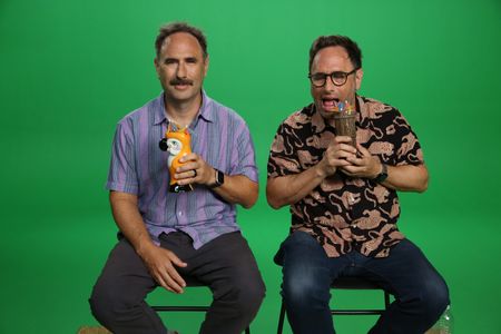 Jason Sklar acting goofy holding a tropical drink sitting Infront of a green screen sitting next to Randy Sklar. (National Geographic/Robert Toth)
