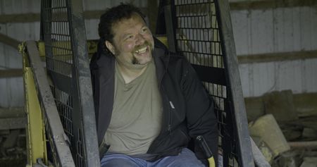 Charles Pol laughs as he sits in his skid steer in his brown pole barn. (National Geographic)