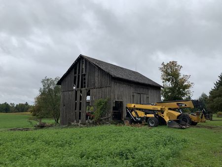 An old barn in Lake, MI that the Pol family plans to take down and restore on the Pol family's farm, with machines and equipment out front. (National Geographic)