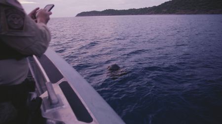 A CBP AMO Agent takes photos on his phone and inspects a floating bag in the water they suspect is carrying drugs. (Lucky 8 TV/Sharon Manente)