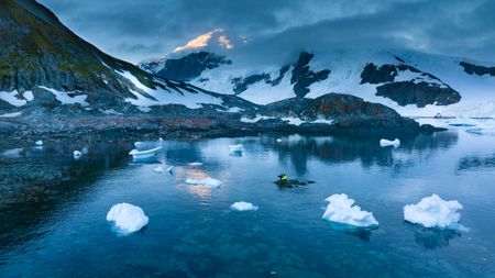 Ralph Bower sits alone on a small rock in the middle of the bay filming Gentoo penguins.  (credit: National Geographic/Bertie Gregory)