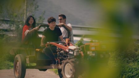 Awkwafina, Junghoon Lee and Antoni Porowski ride the tractor at Cheongdom Farm. (National Geographic)