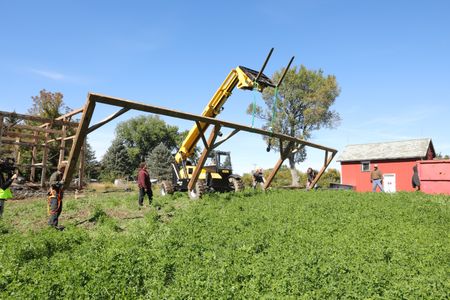 Ben Reinhold, Andrew Hutton, Scott Brady, Seth Doble, Charles Pol, and Bill Klein lower part of the old barn frame down using a telehandler that Scott is operating. (National Geographic)