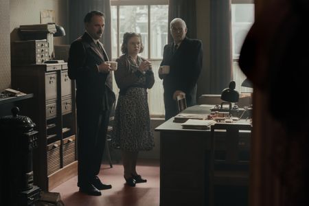 A SMALL LIGHT - Mr. Kugler, played by Nicholas Burns, Bep, played by Sally Messham, and Mr. Kleiman, played by Ian McElhinney, stand in the Opekta office as seen in A SMALL LIGHT. (Credit: National Geographic for Disney/Dusan Martincek)