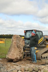 Charles Pol stands by a large rock that was transported from the front yard to the Pol family farm's new pond to be used as a centerpiece. (National Geographic)