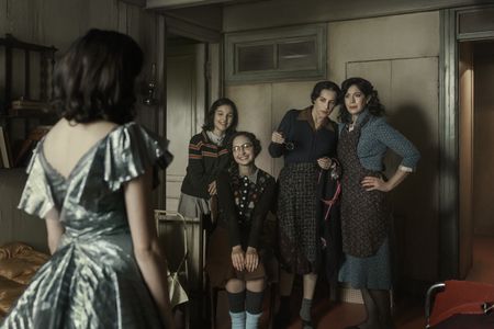 A SMALL LIGHT - Miep tries on a dress for a special event as Anne, Margot, Mrs. Frank and Mrs. van Pels look on, as seen in A SMALL LIGHT. (From left: Bel Powley as Miep Gies, Billie Boullet as Anne Frank, Ashley Brooke as Margot Frank, Amira Casar as Edith Frank, and Caroline Catz as Auguste van Pels). (Credit: National Geographic for Disney/Dusan Martincek)