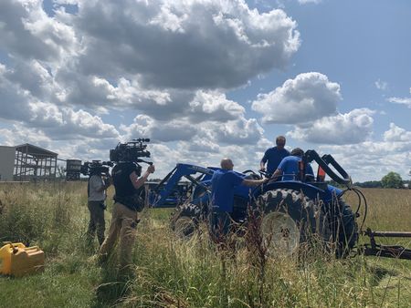 Two crew members film Dr. Pol, Ben Reinhold, and Charles Pol getting the blue tractor ready to condition the hay at the Pol family's farm. (National Geographic)