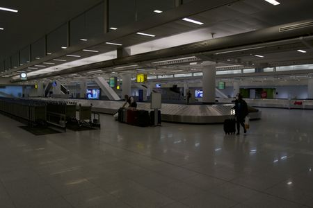 Multiple pieces of luggage are waiting near a baggage claim carousel at the JFK International Airport, as a traveler walks past.(National Geographic)