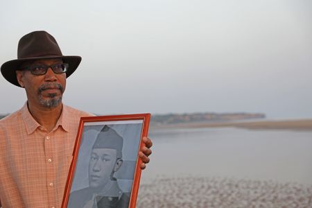 Stephen Woodson holds a picture of his father, Waverly Woodson Jr., while standing on Omaha Beach in France. Waverly Woodson Jr. was a combat medic who served with the 320th Barrage Balloon Battalion on D-Day.  (National Geographic/Shianne Brown)
