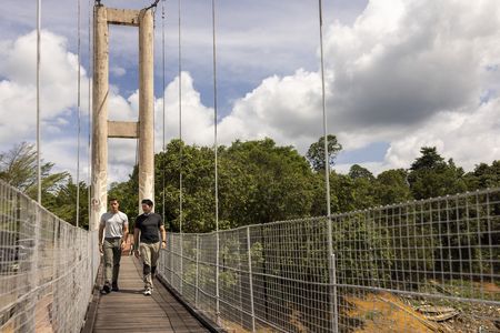 Henry Golding and Antoni Porowski walk a bridge along the river in Bantang Ai. (Credit: National Geographic/Annice Lyn)