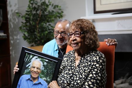 Vinnie and Beulah Dabney, son and wife of William Dabney, respectively, are pictured holding a framed portrait of Dabney Sr. while at their home in Roanoke, Va. Corporal William Dabney served with the 320th Barrage Balloon Battalion on D-Day. (National Geographic/Shianne Brown)