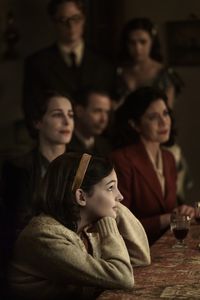 A SMALL LIGHT - The Frank, van Pels, and Gies families celebrate Hanukkah in the secret annex, as seen in A SMALL LIGHT. (Clockwise from top: Joe Cole as Jan Gies, Bel Powley as Miep Gies, Caroline Catz as Auguste van Pels, Billie Boullet as Anne Frank, Amira Casar as Edith Frank, and Noah Taylor as Dr. Pfeffer). (Credit: National Geographic for Disney/Dusan Martincek)