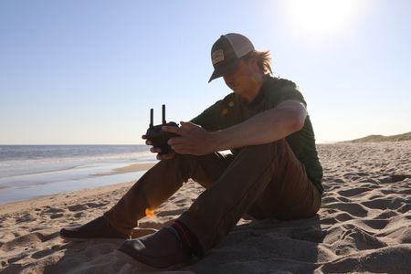 Tim Regan sat on the beach and holding the controller for his drone. (National Geographic/Mariana Kneppers)