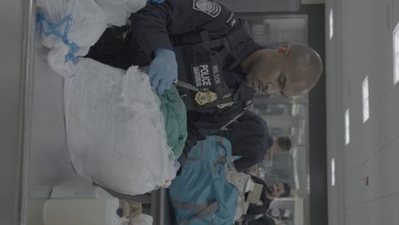 CBP Officer Wilson inspects a package found in a courier's belongings in Dulles, Va. Fellow officers Hundal and Augustino perform other inspetions in the background. (National Geographic)