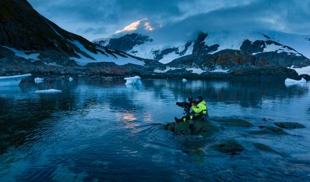 Ralph Bower sits alone on a small rock in the middle of the bay filming Gentoo penguins.  (credit: National Geographic/Bertie Gregory)