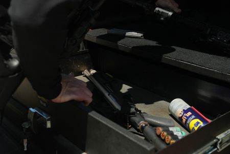 A CBP Agent unloads ammunition and weaponry from the trunk of a vehicle with a Remington shotgun laying down in the foreground of the trunk in St Thomas, USV. (Lucky 8 TV)