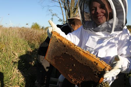 Beth Pol, in a bee suit, smiles while holding a frame from the farm's beehive, while checking on the hive before winter. (National Geographic)