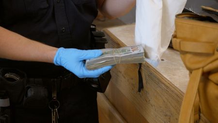 CBP Officer Papa holds a stack of cash as he tries to determine the amount of currency found in a traveler's belongings in El Paso, Texas. (National Geographic)