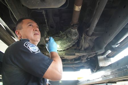 CBP Officer Vasquez uses a flashlight to inspect the underside of a suspect's vehicle for smuggled narcotics in Pharr, Texas. (National Geographic)